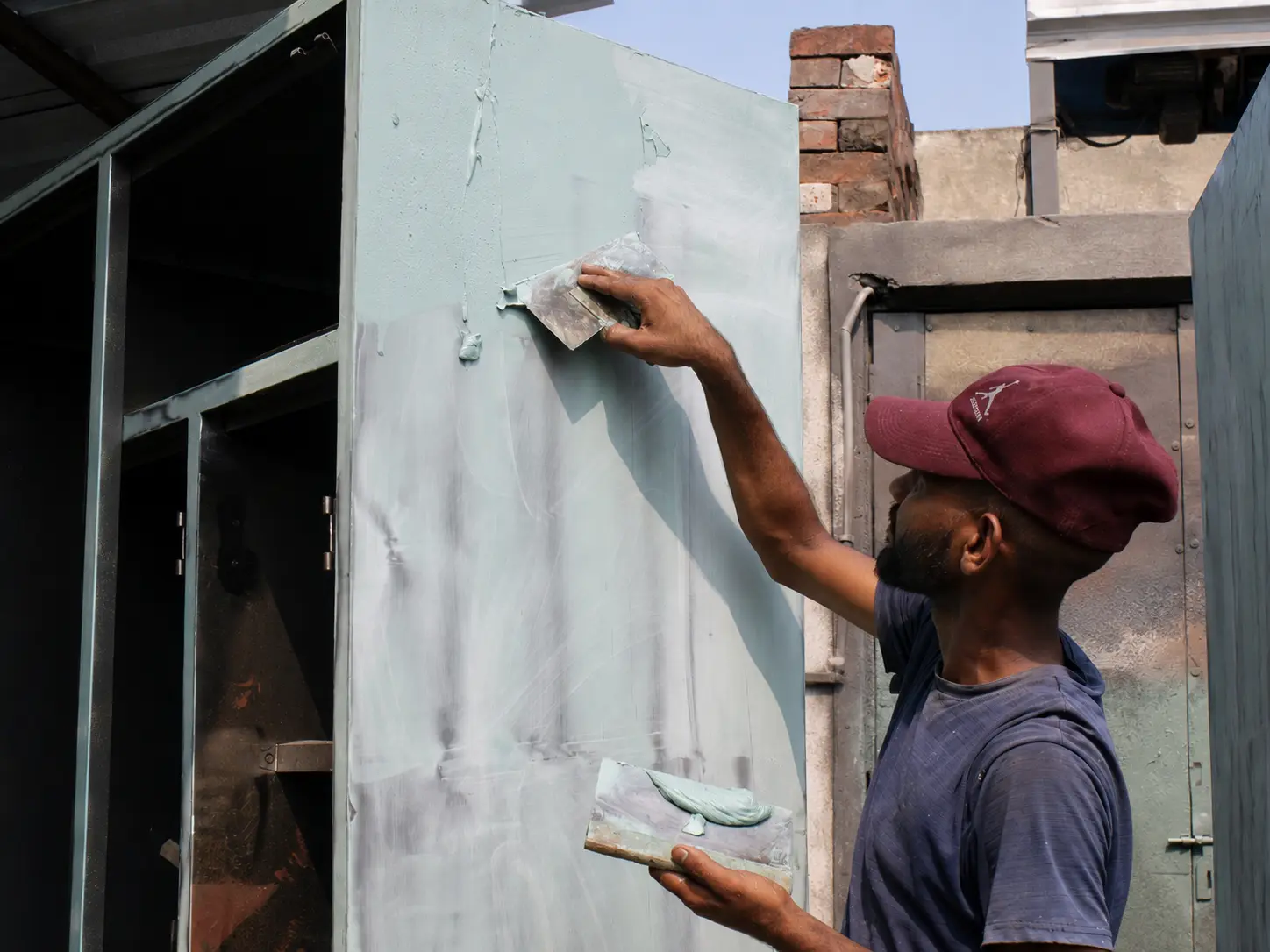 Craftsperson applying putty to a steel almirah surface